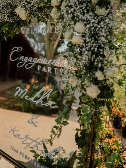 A welcome mirror for an engagement party, elegantly scripted and framed with baby's breath and roses.