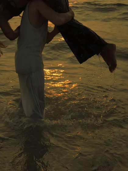 The warm, golden light reflecting on the water adds a magical quality to this photo. This is a detail from a sunset session, focusing on the movement and joy of the moment.