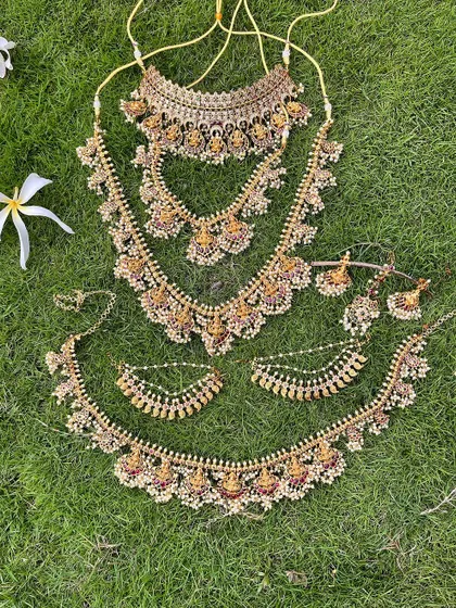 A full view of a temple jewellery set with pearl detailing, laid out on the grass. This shows the choker, two haarams, and the vaddanam.