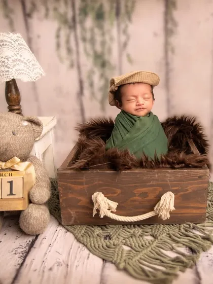 Dream big, little one. This setup features a baby in a wooden suitcase with a teddy bear holding a date block, suggesting the start of a great adventure.