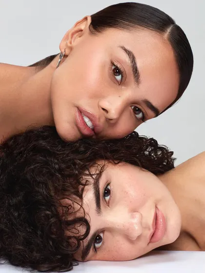 An intimate and artistic portrait of two models. The composition emphasizes natural skin and close connection, suitable for a brand that promotes authentic and inclusive beauty.