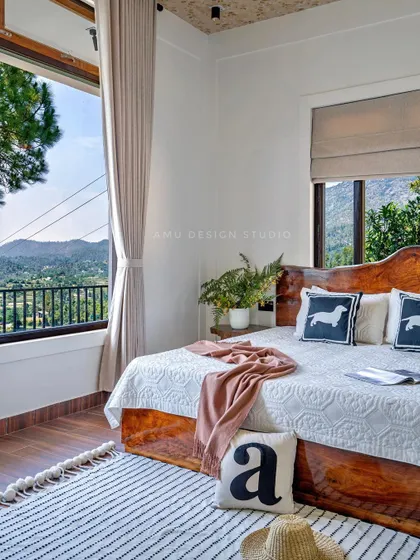 A guest bedroom in 'The Mountain Home,' designed for comfort and simplicity. The room features a solid wood bed, large windows, and minimal decor to keep the focus on the stunning natural landscape outside.