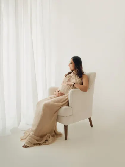 A moment of quiet reflection. Using simple props like this armchair and soft window light, we can create serene and thoughtful maternity portraits.