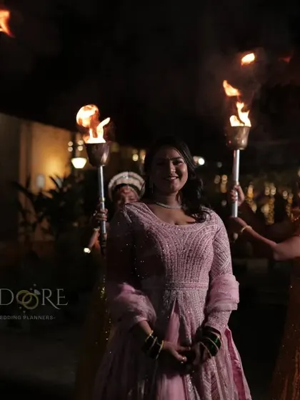 The bride making her stunning entrance for the reception, surrounded by the warm glow of fire torches held by traditionally dressed performers.