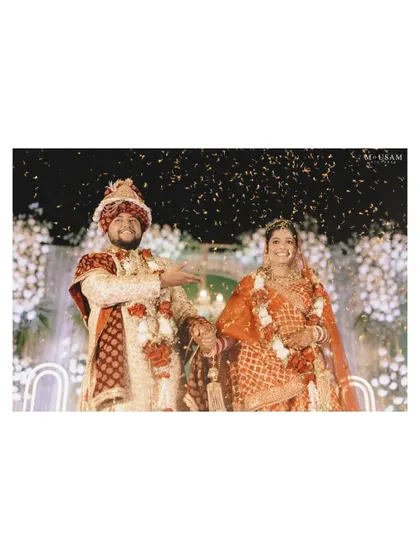 The couple on stage during their Varmala ceremony, showered with confetti. Their happy smiles show the joy of this milestone moment, surrounded by the grand celebration.