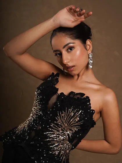 This pose highlights the statement earrings and the beautiful neckline of the designer top. The soft studio lighting creates a gentle glow on the skin.