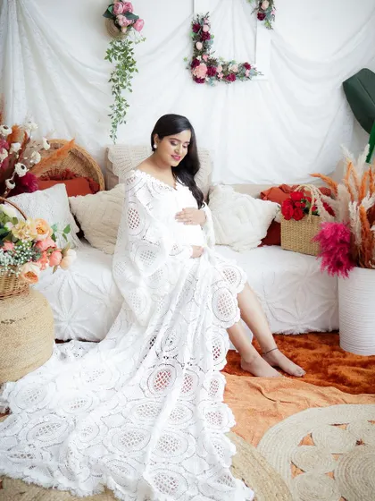 A beautiful and serene portrait in a boho-chic setting. The mom-to-be is dressed in a delicate white lace gown, her expression full of peace.