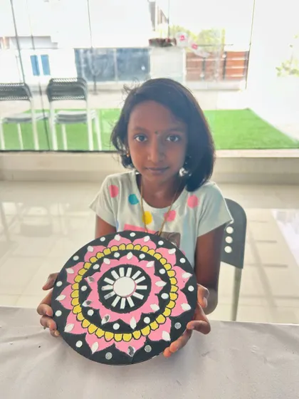 A young girl proudly holds up the colorful Lippan art mandala she created in our studio.