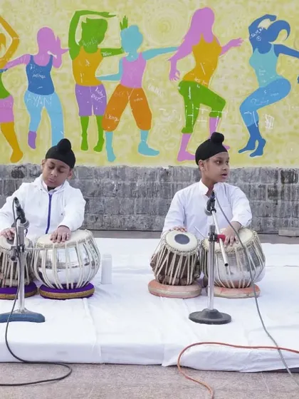 A focused shot of two young students playing tabla in unison during a public performance.