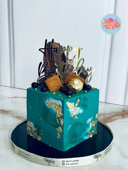 A modern, square-tiered cake in a beautiful teal, with gold leaf accents and Ferrero Rocher chocolates.