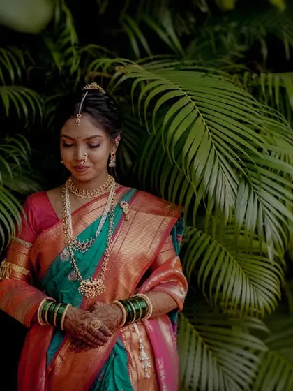 A serene portrait of the bride in her beautiful saree, standing amidst lush palm fronds, a moment of calm before the ceremony.