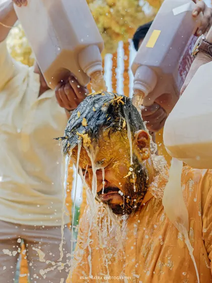 A close-up shot captures the sheer fun of the Haldi as the groom is drenched in milk and turmeric.