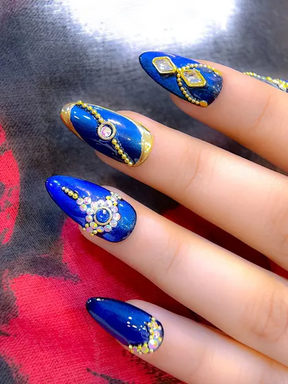 A close-up of the royal blue Navratri nails, showing the detailed placement of gold beads and multi-sized crystals to create ornate patterns.