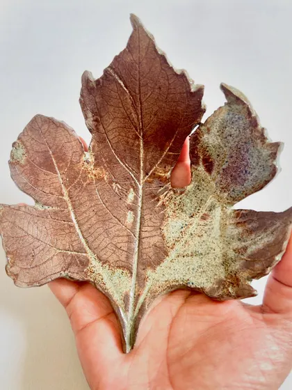 Holding a hand-built ceramic leaf, you can see the rustic, earthy finish from the glaze.