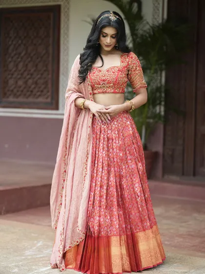 A full view of the coral-red brocade half saree, showcasing the beautiful fall of the lehenga and the elegant drape of the tissue dupatta.