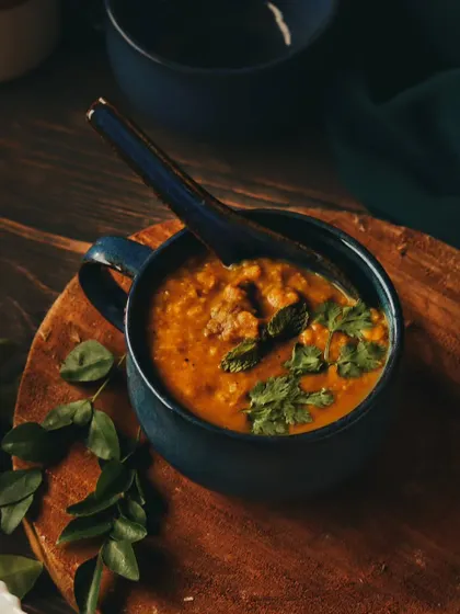 A comforting bowl of Daleem, a traditional slow-cooked stew, garnished with fresh herbs. The moody lighting and rustic wooden board create a warm and hearty feel, perfect for showcasing traditional cuisine.