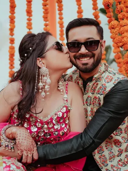 A cute and playful moment at the Mehendi, with the bride giving the groom a kiss on the cheek as they pose on a decorated swing.