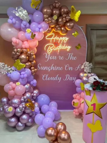 A personalized first birthday backdrop with a touching message. This setup features a pastel and chrome balloon arch with butterfly details and a custom sign.