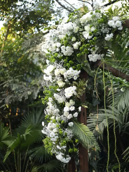 A close-up of the floral arrangement on the wooden ceremony arch, showcasing the mix of white flowers and fresh green leaves.
