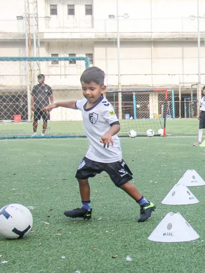 A young player dribbles through a series of cones, demonstrating the focus and coordination we build through our age-specific training programs.