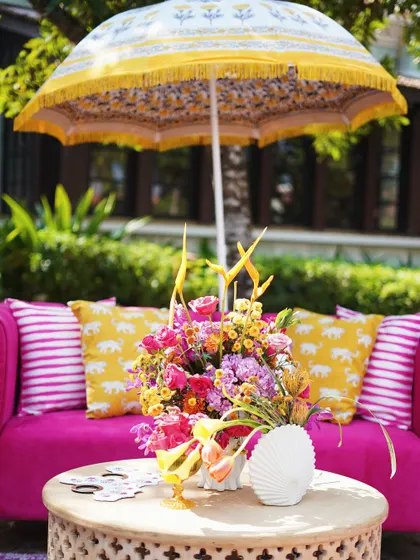 For a fun and vibrant Haldi, I designed this seating area with a bright pink sofa, elephant-print cushions, and a colorful floral arrangement under a traditional yellow umbrella.