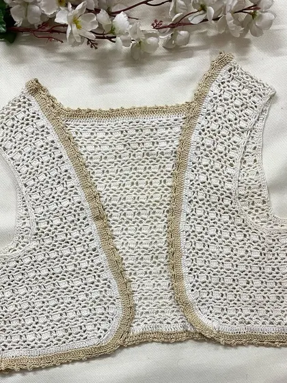 A closer look at our sleeveless shrug in white with a beige border. It's a simple and elegant piece to layer over tops and dresses.