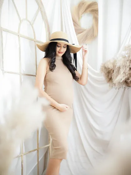 A duplicate of image 126, this chic portrait features a mom-to-be in a simple beige dress and sun hat, creating a timeless and elegant look.