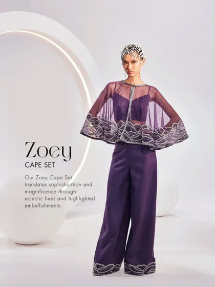The Zoey Cape Set in a regal purple. This ensemble features a sheer embellished cape paired with a simple bustier and wide-leg trousers for a look of magnificent sophistication.