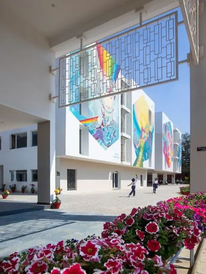 A view through a decorative metal screen frames the colorful school facade. These screens provide shade and visual interest, demonstrating how transitional spaces can enhance the overall architectural experience of the campus.