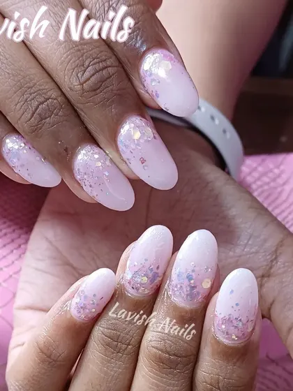 A soft, light pink base on almond-shaped nails with a gentle scattering of iridescent glitter flakes for a subtle, magical effect.