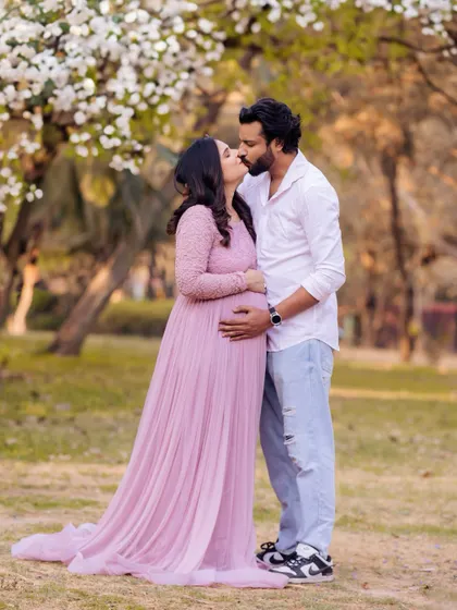 A sweet kiss shared between the couple during their outdoor maternity shoot. The blooming white flowers on the trees behind them add to the romantic and fresh feeling of the portrait.