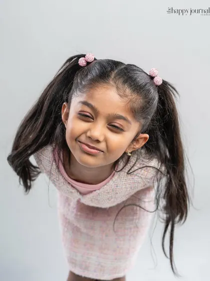 A playful and cute shot of a girl in a pink outfit, squeezing her eyes shut with a happy, mischievous smile.