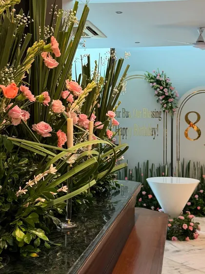 A wider view of the 80th birthday setup, showing how the floral arrangements on the bar connect with the main backdrop in the background, creating a cohesive and immersive environment.