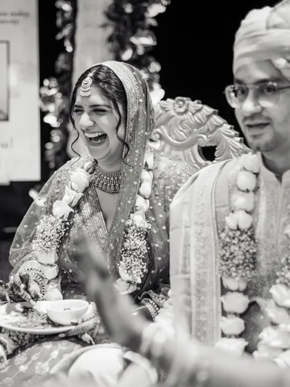 A candid black and white shot of the bride's infectious laughter during a wedding ritual, showing the joy and spontaneity of the day.