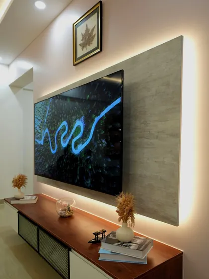 An angled view of the TV unit, showing how the warm backlighting highlights the textured panel and creates a floating effect. The minimalist decor keeps the focus on the personal and artistic elements.