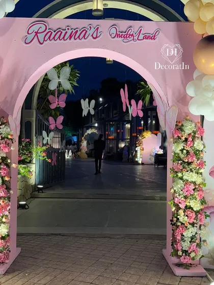 A close-up of the entrance archway, detailed with floral pillars and hanging butterflies, creating a magical portal into the party.