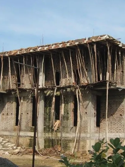 An on-site construction image of a residential building. This photo shows the brickwork and concrete structure, with temporary wooden scaffolding supporting a newly cast roof slab.