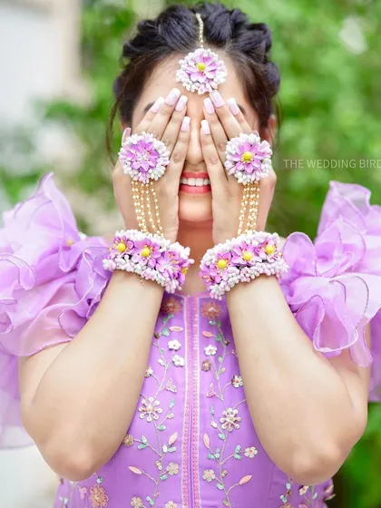 A playful mehendi portrait. The bride hides her smiling face behind her hands, showing off her beautiful floral jewelry and the joy of the occasion.