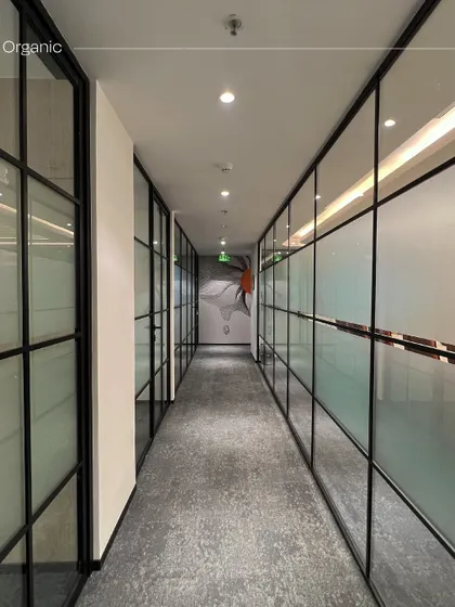 A corridor in the Rays Power office lined with glass-walled cabins. The use of frosted and clear glass panels provides privacy while still allowing natural light to flow through the space, creating a sense of openness.