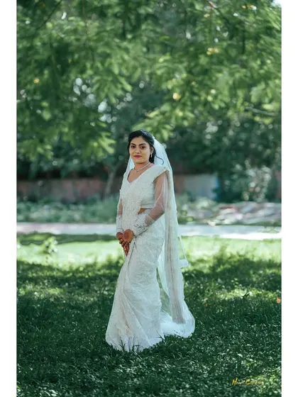 A portrait of a Christian bride in her beautiful white saree-style gown, standing in a serene garden.