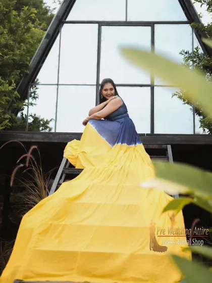 The blue and yellow trail gown drapes down a set of stairs, highlighting the length of the tail and the beautiful color gradient.