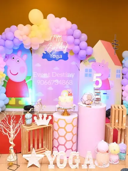 A playful Peppa Pig theme for a 5th birthday. The decor includes a backdrop of Peppa's house, character cutouts, and a colorful pastel balloon arrangement.