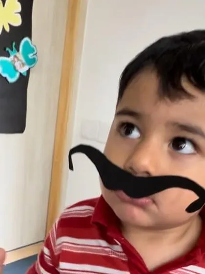 A child playfully wears a mustache prop as part of our La Tomatina celebration.