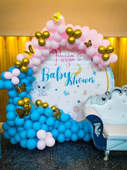 A cute and modern baby shower decoration with a blue and pink balloon arch and an elephant-themed backdrop.