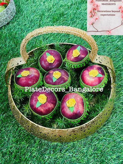 Red apples decorated with green bases and yellow roses, presented in a hammered gold-tone basket.