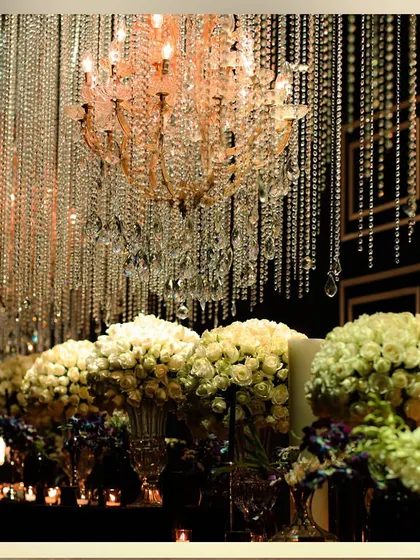 A long bar or buffet table lined with white rose bouquets and candles, under a ceiling of hanging crystals. This creates a stunning visual display.