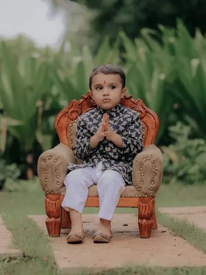 A sweet 'namaste' from this little one. This pose, combined with his traditional attire, makes for a respectful and heartwarming portrait during his outdoor baby shoot.