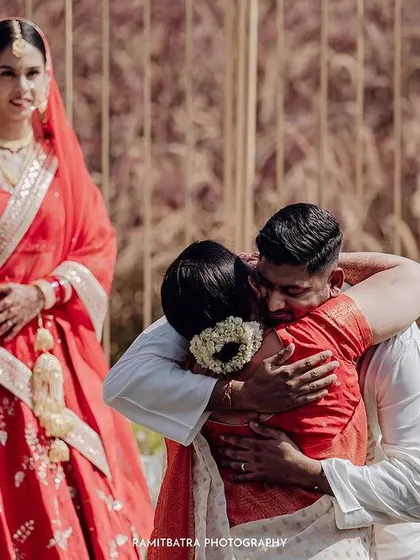 An emotional moment during the wedding ceremony as the groom hugs a family member, with the bride looking on.