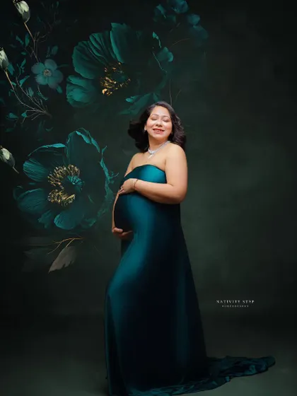 A fine art portrait in a teal gown against a dark, floral-painted backdrop. The mother's serene expression adds to the artistic quality of the shot.