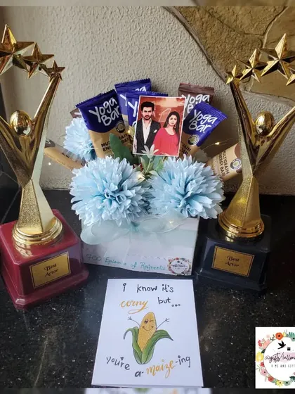 A custom bouquet and trophy set to celebrate 700 episodes of the show 'Parineetii'. The bouquet is filled with protein bars and decorated with blue flowers.